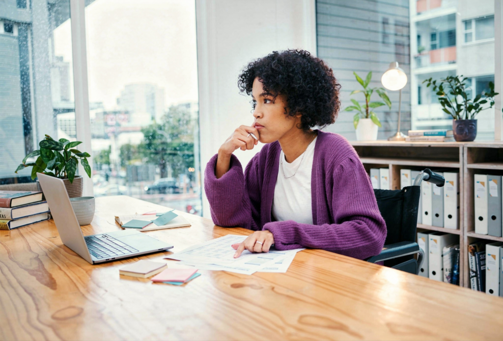 Woman sitting at desk with laptop thinking.