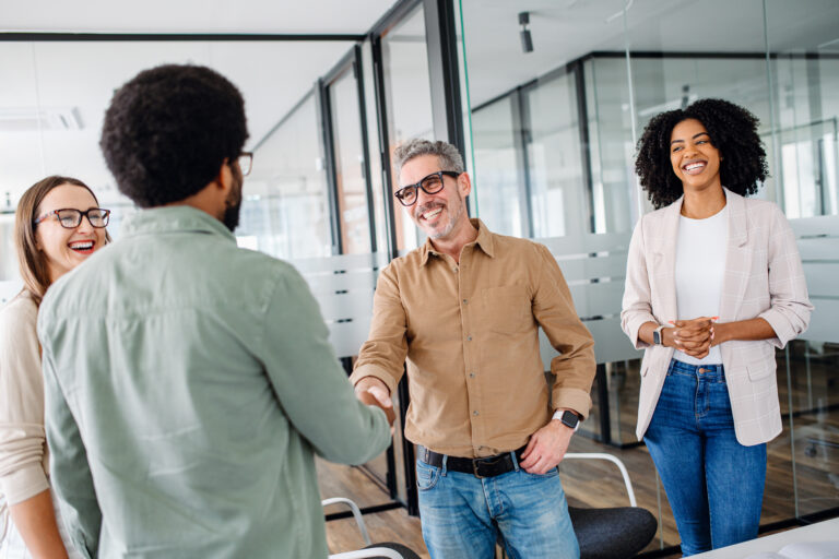 Friendly office environment is depicted where team greets each other shaking hands